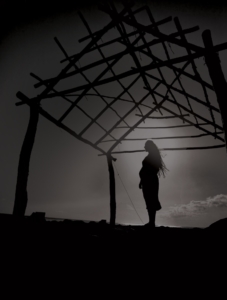 Photo: Wahine standing near a traditional Hawaiian building